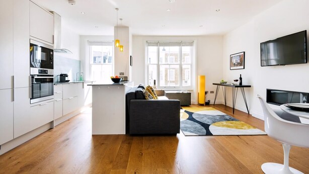 Eine moderne Küche mit weißen Schränken, einem eingebauten Ofen und einer Mikrowelle. Es gibt einen Essbereich mit Tisch und Stühlen sowie ein Sofa in der Mitte.