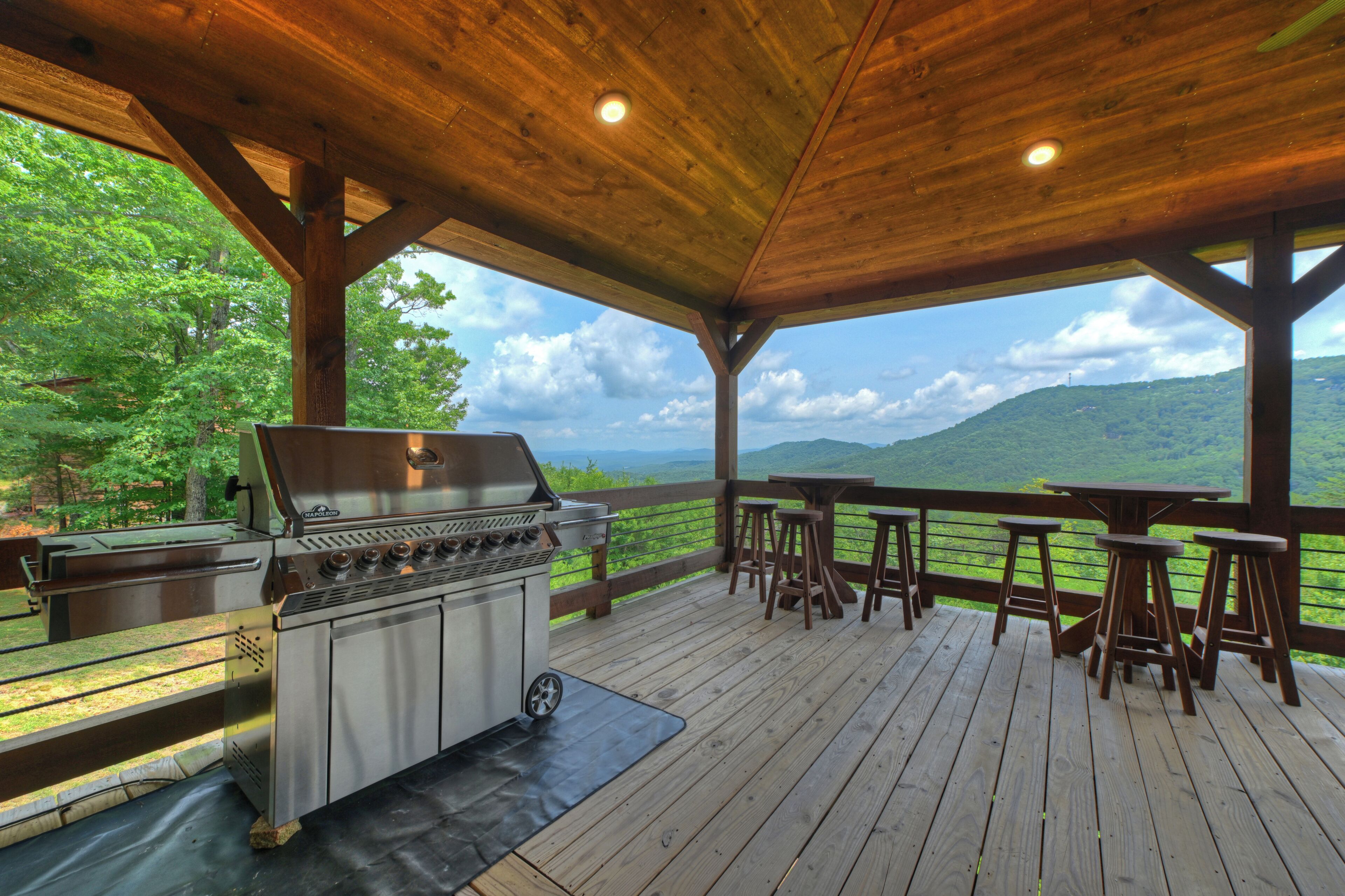 Un espacio al aire libre techado con una parrilla, terraza de madera y vistas a un paisaje montañoso.