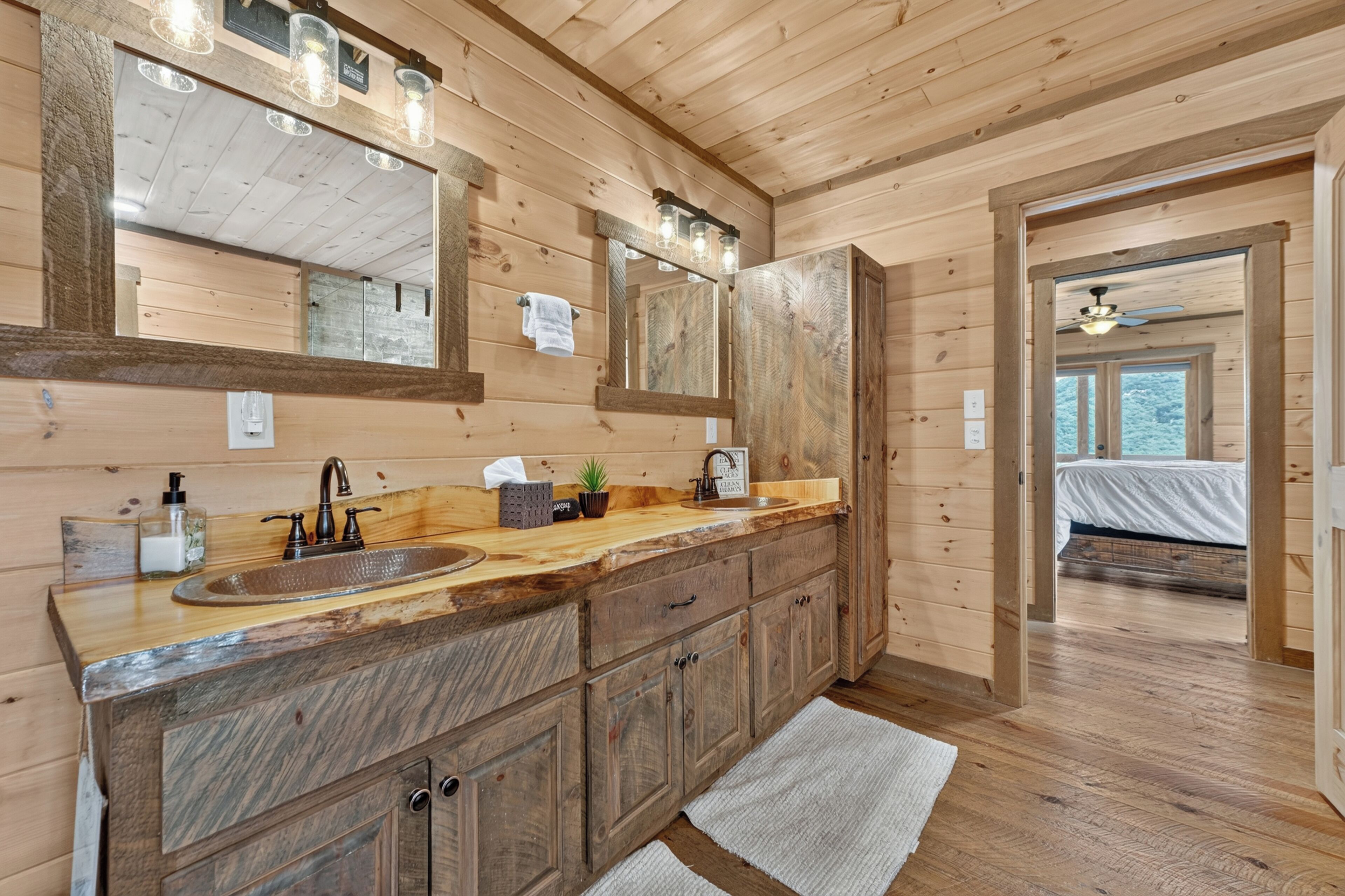 A wooden cabin interior with a large mirror, a sink, and a bed visible through an open doorway.