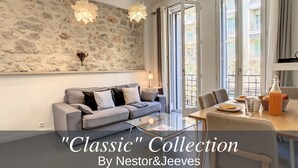 Ein modernes Wohnzimmer mit Steinwand, grauem Sofa, Glastisch und einem Essbereich mit Tisch und Stühlen.