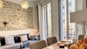 Ein modernes Wohnzimmer mit Steinwand, einem grauen Sofa, einem Esstisch mit Frühstücksgebäck und großen Fenstern.