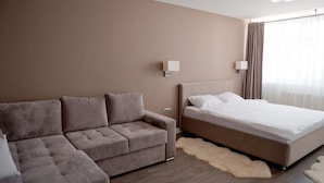 Ein modernes Hotelzimmer mit einer Couch, einem Bett und einem großen Fenster mit Vorhängen.
