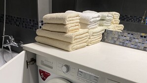Ein kompakter, moderner Waschraum mit einer Waschmaschine mit Frontlader, einem Stapel weißer Handtücher und einer kleinen Ablage für Toilettenartikel.