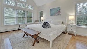 A bedroom with a large bed, a bedside table, a chair, and a window with blinds.