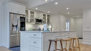 A modern kitchen with white cabinetry, stainless steel appliances, and wooden stools.