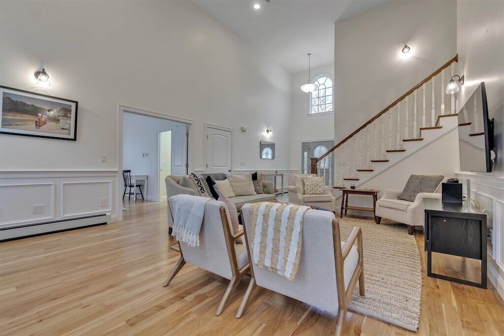 A spacious living room with a high ceiling, a staircase, and a dining area.