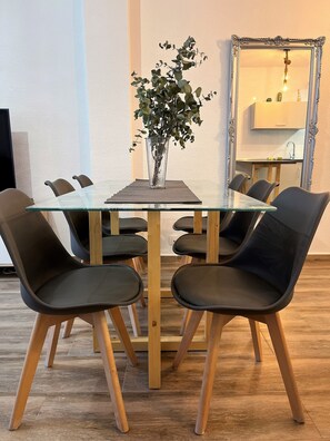 A modern dining area with a glass table, black chairs, and a potted plant.