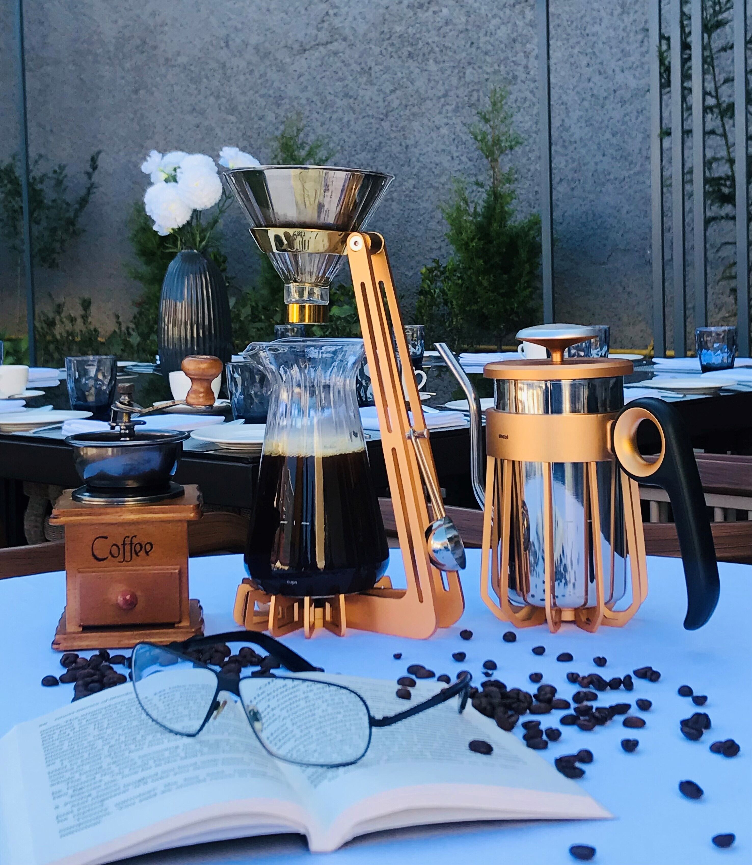 Une table avec du matériel pour préparer le café, un livre et des grains de café éparpillés.