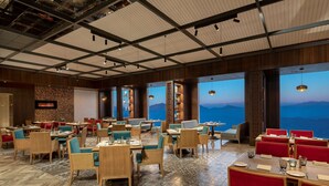 A spacious restaurant with multiple seating areas, a large TV screen, and a view of the mountains. - Radisson Hotel Kufri Shimla (Theog)