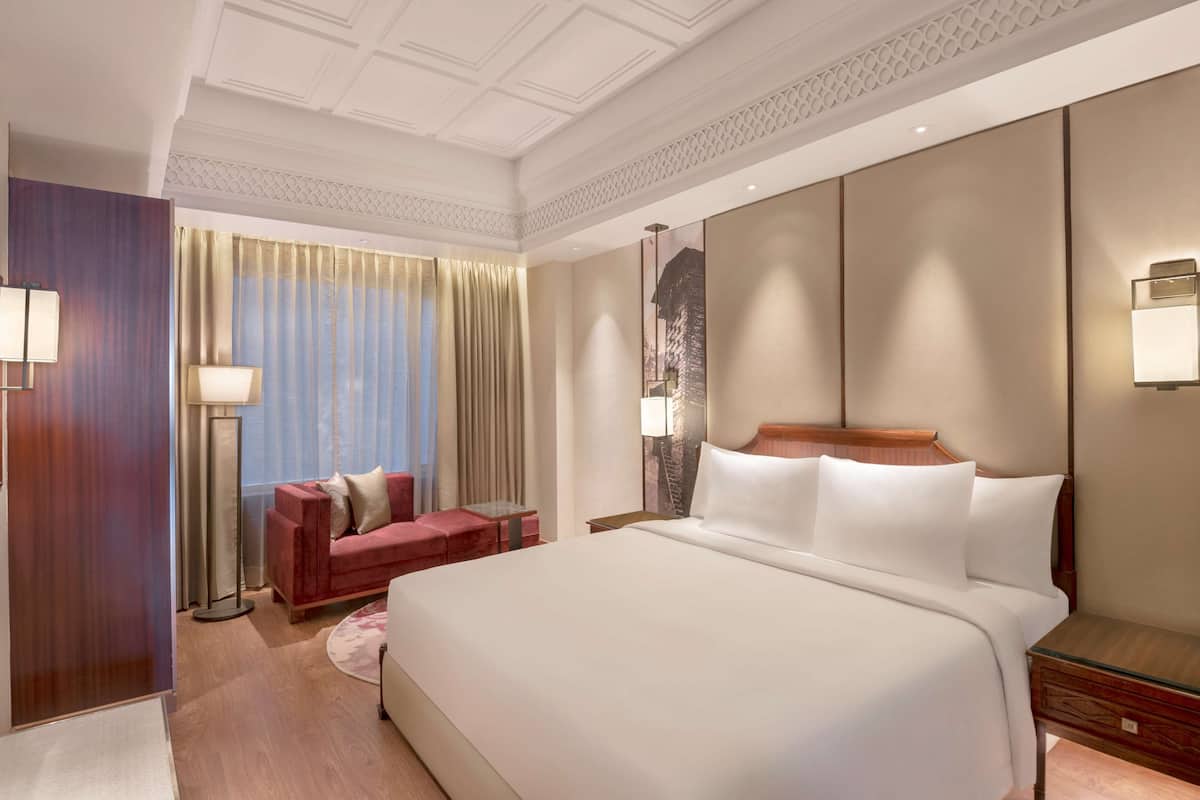 A hotel room with a large bed, a red sofa, a standing lamp, and a decorative wall piece.
