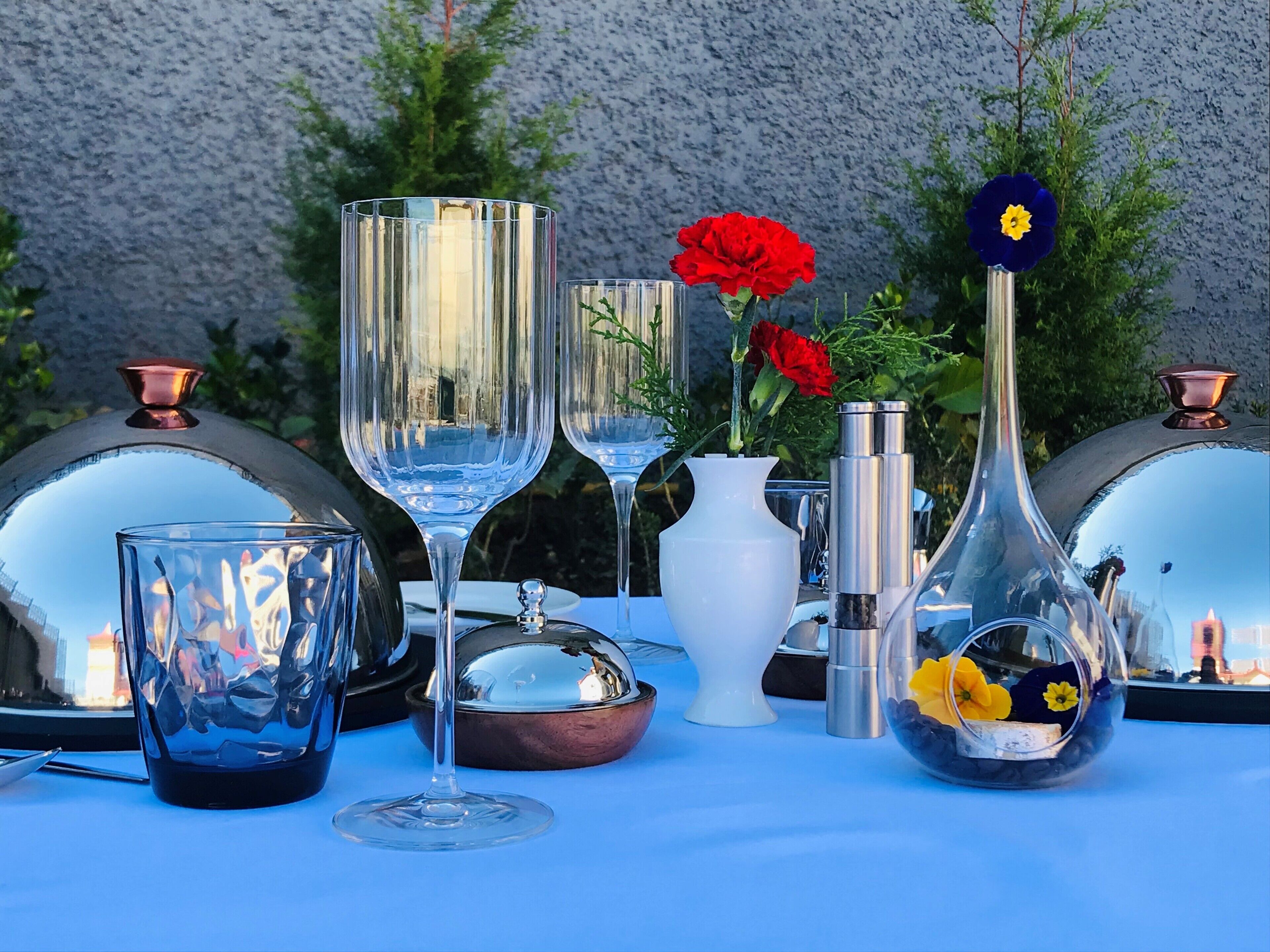 A table with various glassware and vases, including a white vase with red flowers and a clear vase with yellow flowers.