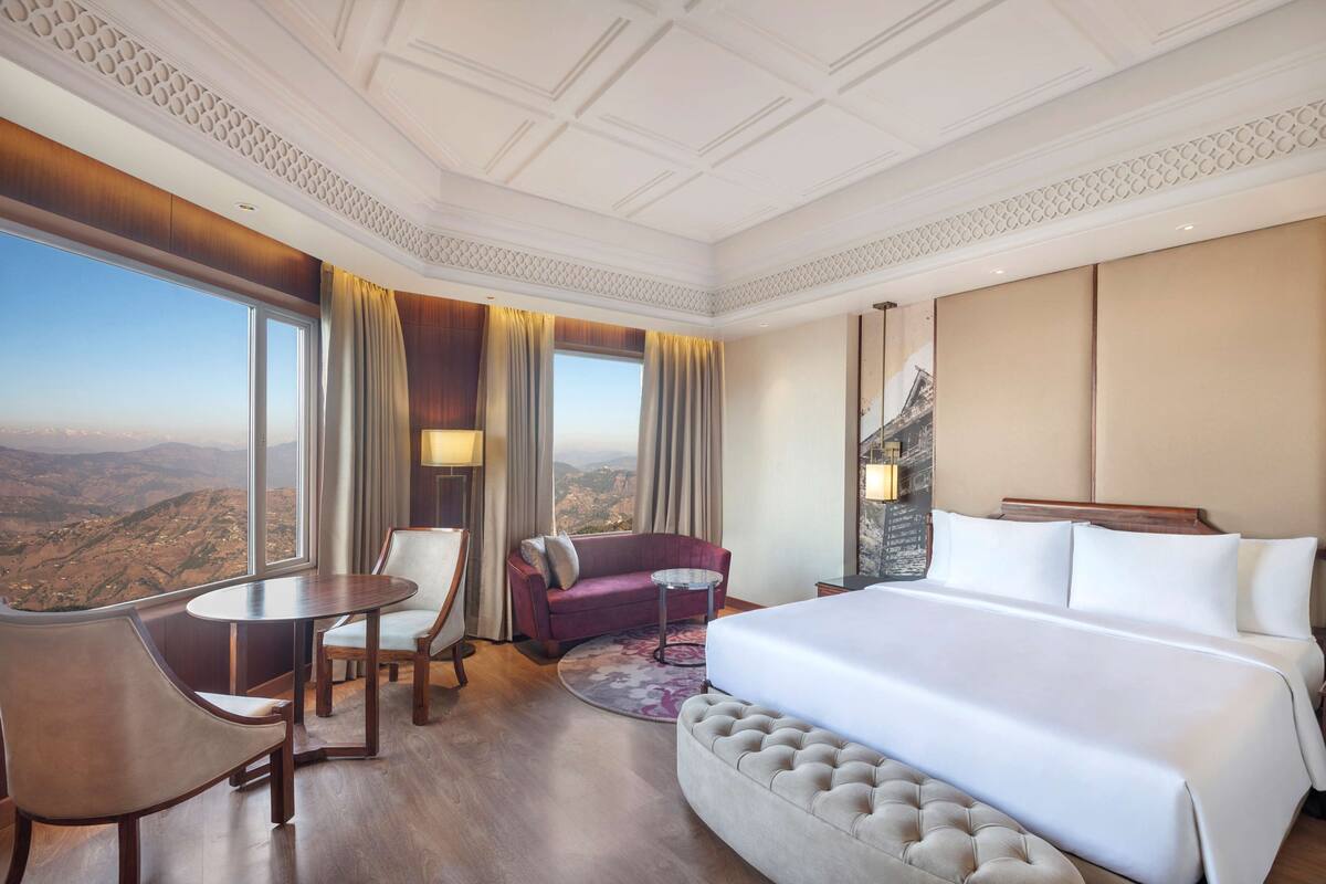 A hotel room with a large bed, a sofa, a dining table, and a view of the mountains.