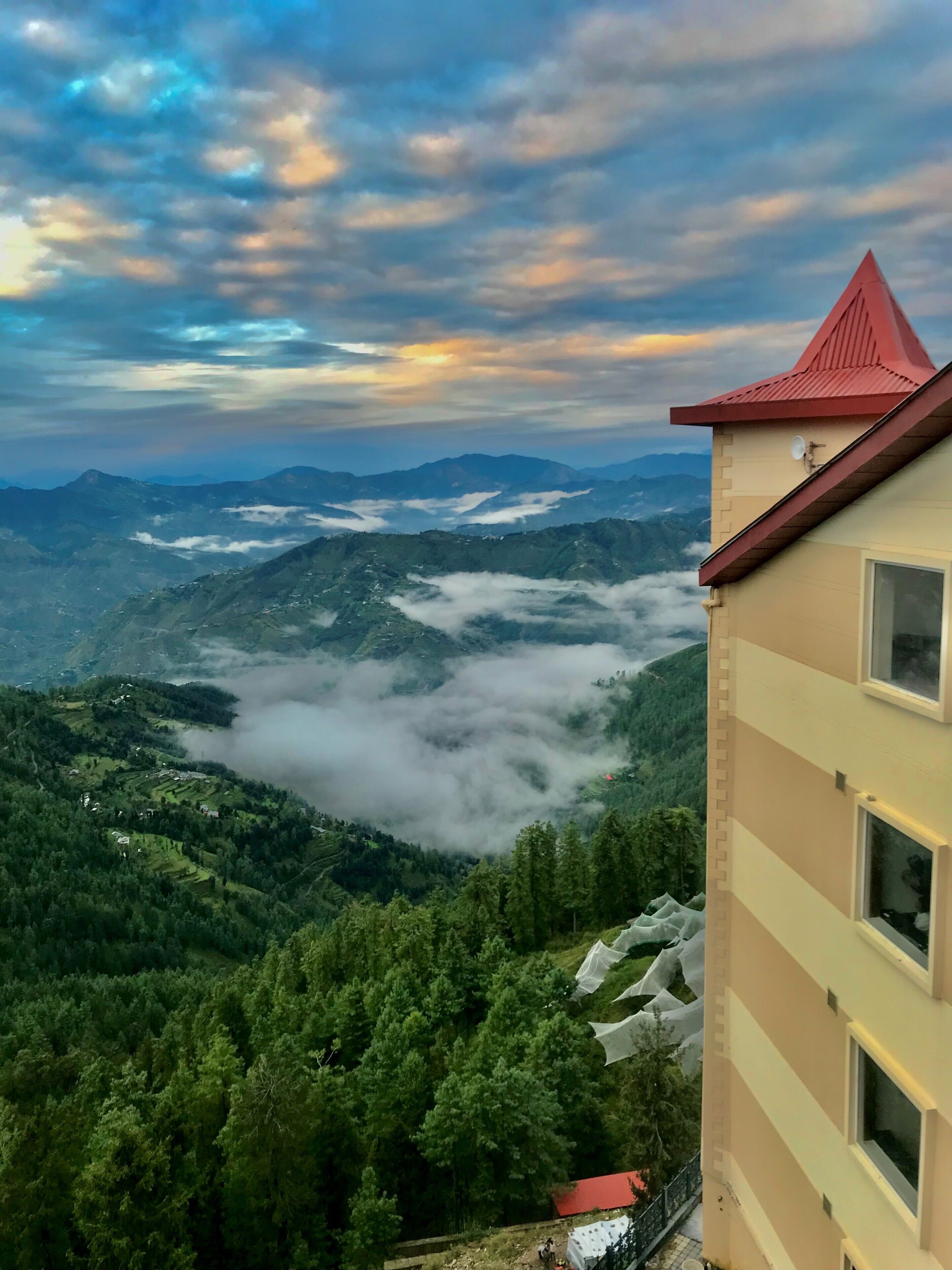 Une vue sur une montagne, avec un bâtiment doté d’un toit rouge et de nombreuses fenêtres.