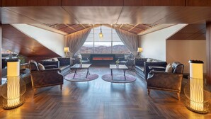 A spacious lounge area with leather sofas, round tables, and floor lamps. A large window offers a view of mountains. - Radisson Hotel Kufri Shimla (Theog)