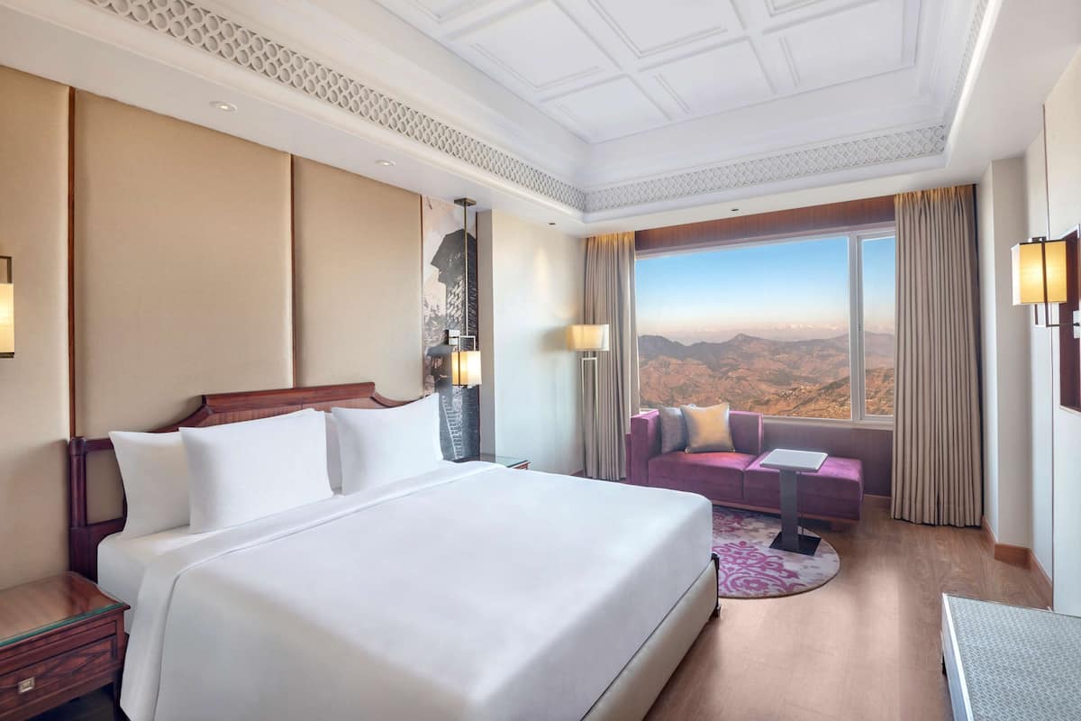A hotel room with a large bed, a sofa, a desk, and a view of the mountains.