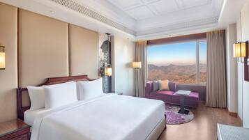 A hotel room with a large bed, a sofa, a desk, and a view of the mountains.