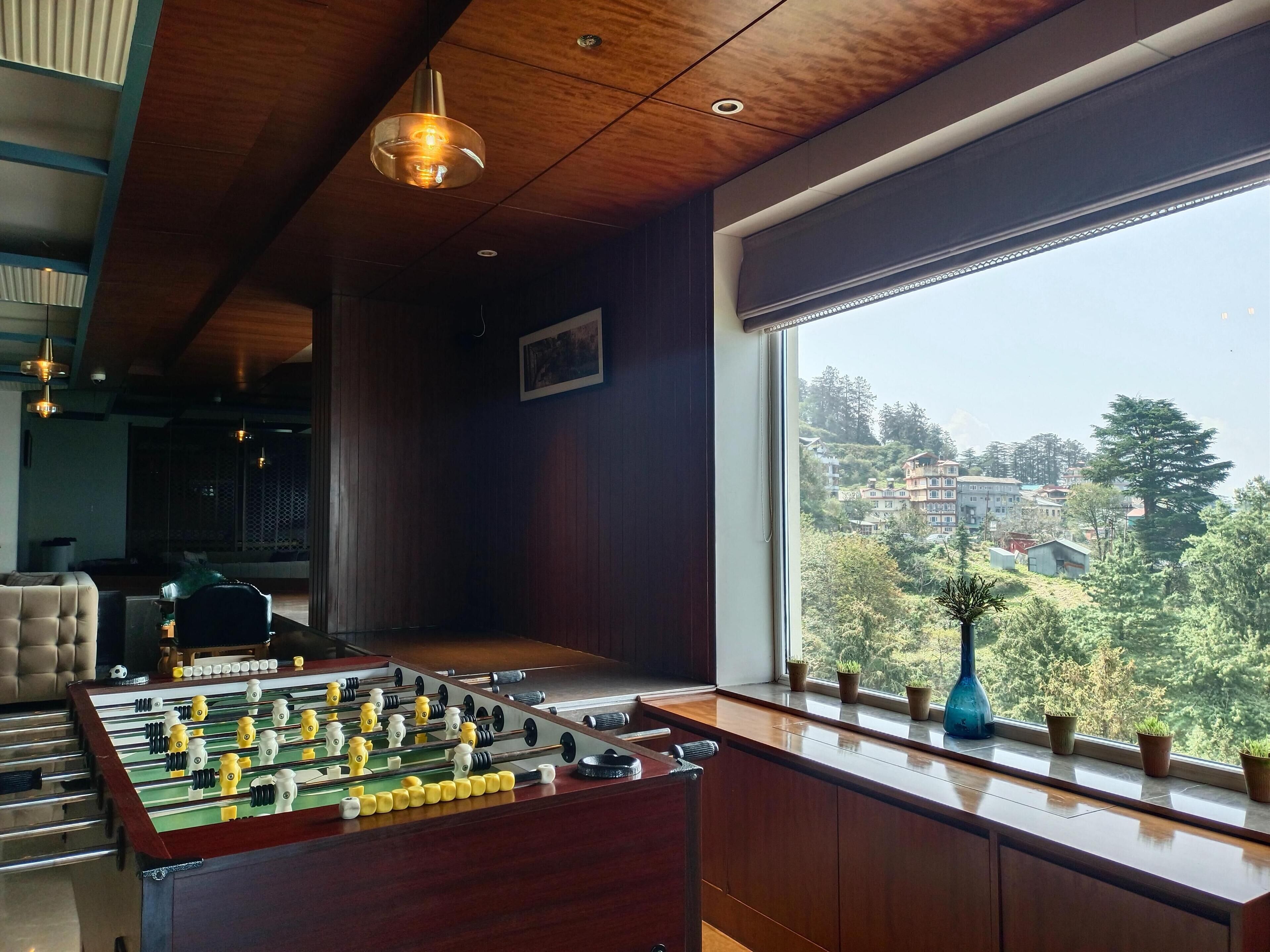 A room with a foosball table, a window with a view of a hillside, and a wooden ceiling.