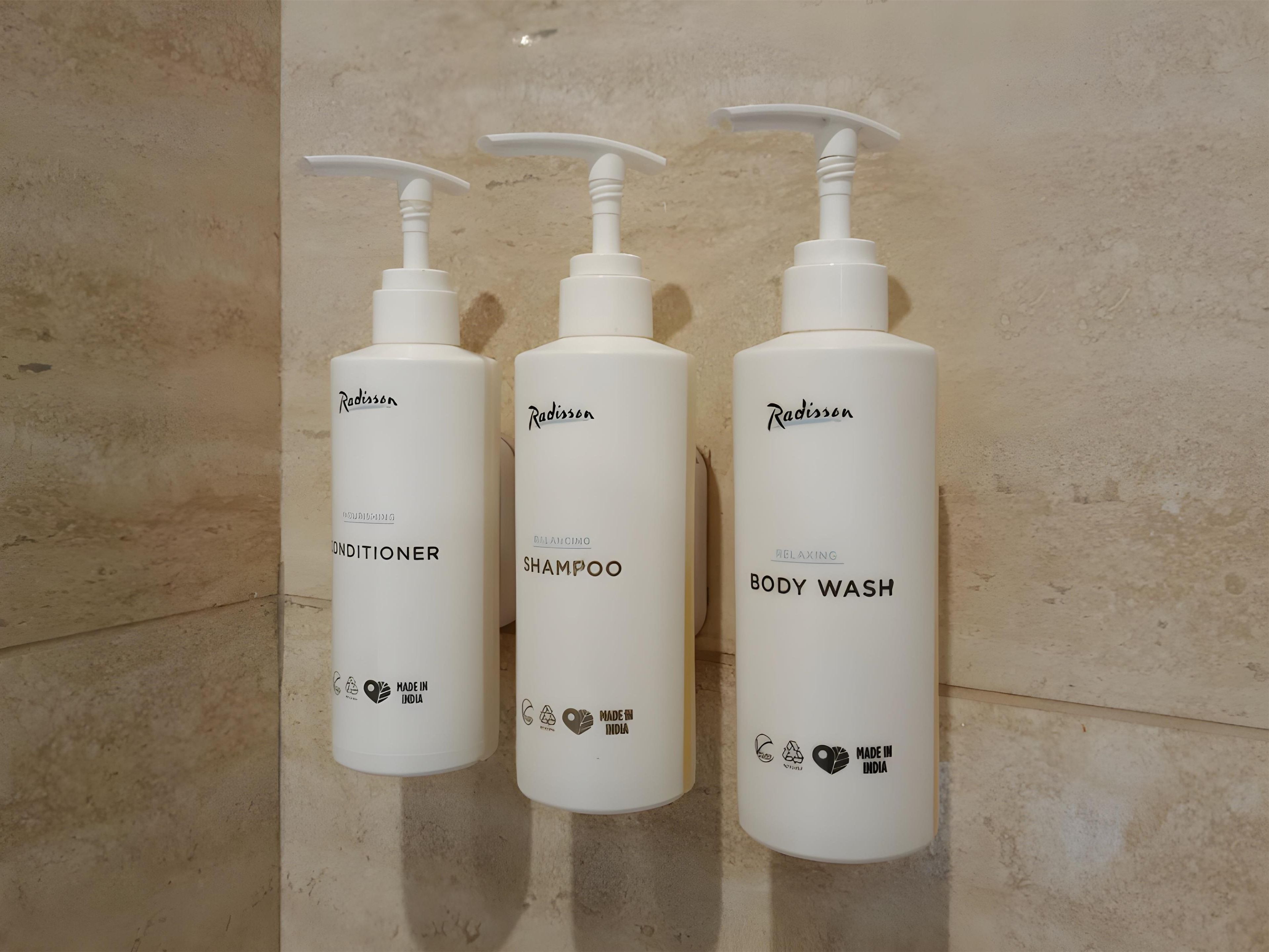 Three white bottles of Radisson toiletries on a tiled wall.