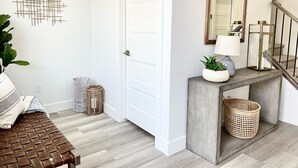 A modern hallway with a wooden bench, a decorative wall piece, a console table with a mirror and lamp, and a staircase. - New TownHome w/ Heated Pool & Hot Tub in St.George (St. George)
