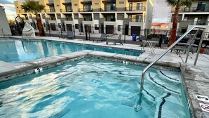 A swimming pool with a tiled deck, a metal ladder, and a building with balconies in the background. - New TownHome w/ Heated Pool & Hot Tub in St.George (St. George)