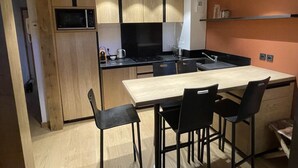 A modern kitchen with wooden cabinets, a black countertop, and a wooden dining table with four chairs. - Le Jardin Alpin: Cozy apartment in a luxury residence (Les Deux Alpes)