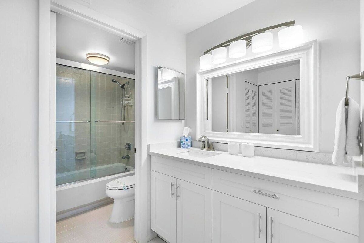 A modern bathroom with a glass-enclosed shower, a white sink with a large mirror, and a toilet.