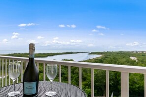 A bottle of Prosecco wine and two glasses on a balcony with a view of a body of water and greenery. - South Seas Retreat Beachfront 2BD/2BA- Gulf Views (Marco Island)