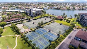 Complejo de canchas de tenis con varias canchas, rodeado de edificios y una masa de agua.