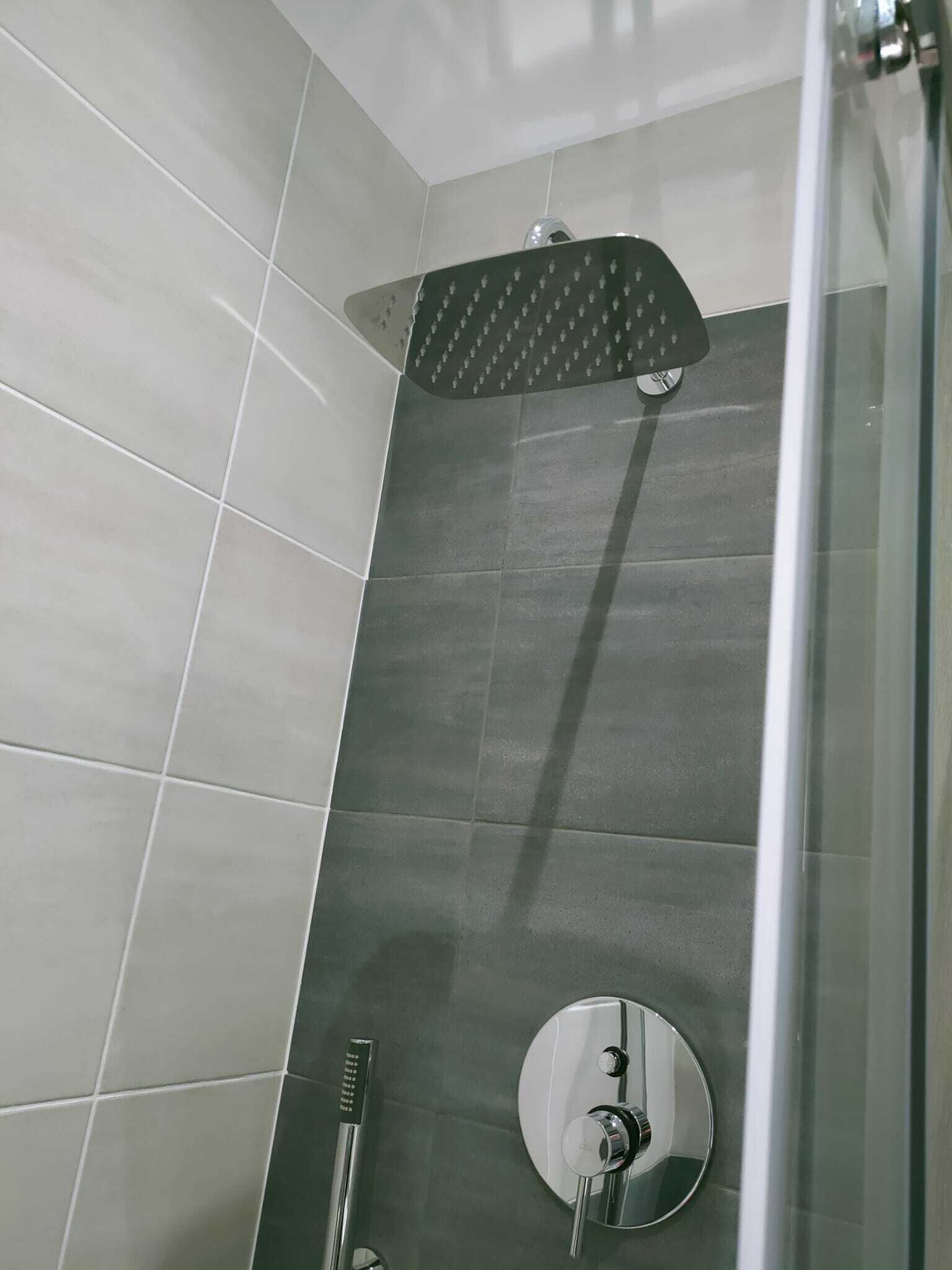 Un espace douche doté d’une porte en verre, d’un pommeau de douche à main et d’un miroir rond.