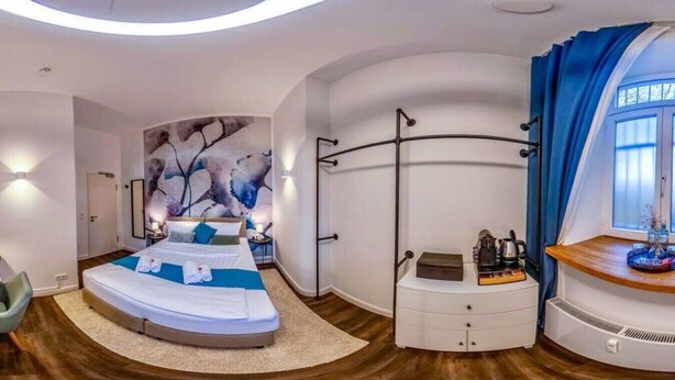 Een moderne slaapkamer met een gebogen plafond, een groot bed, een nachtkastje, een dressoir en een raam met gordijnen.