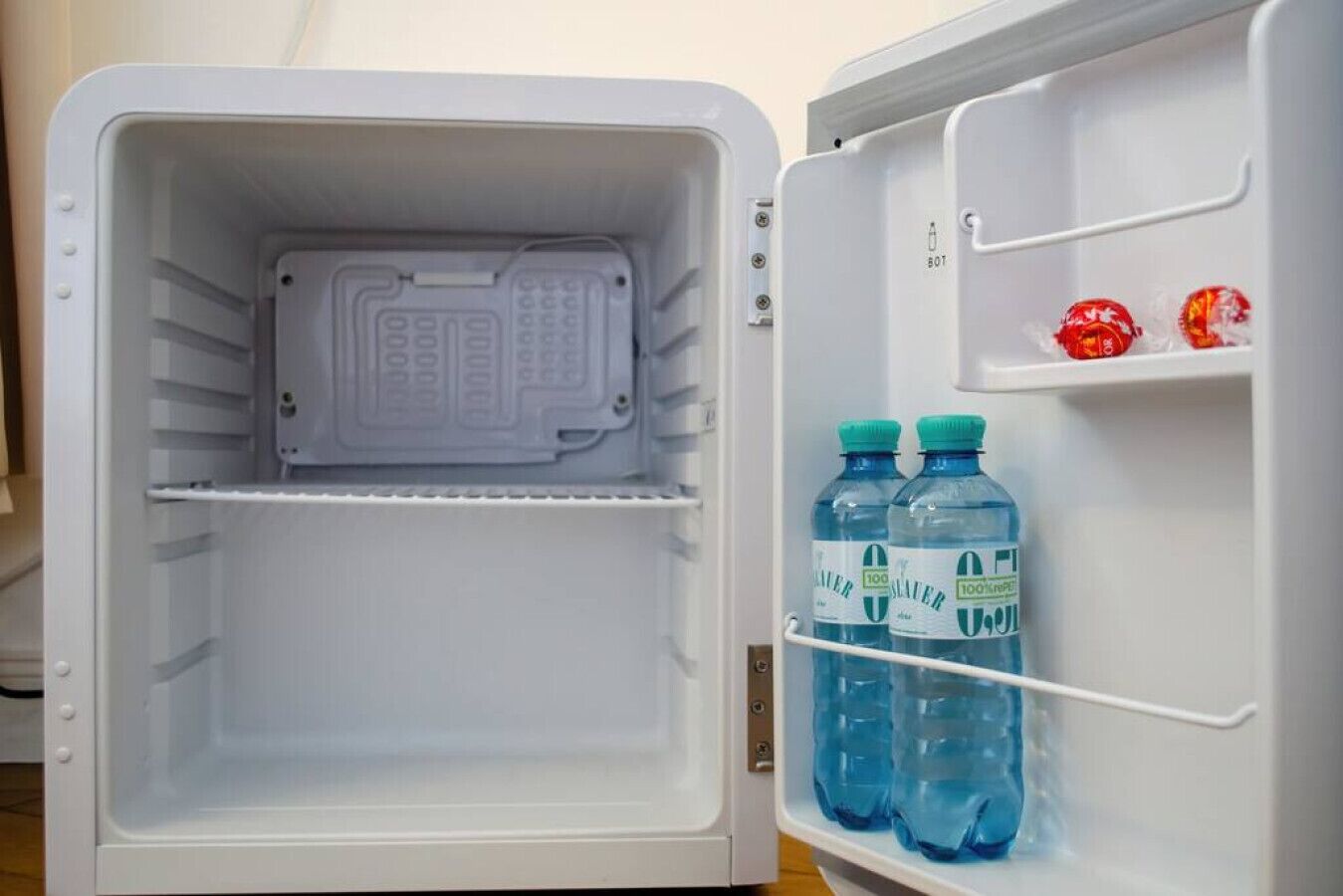 An open refrigerator with a water dispenser and two bottles of water on the door shelf.