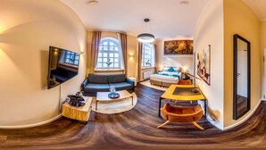 A modern living room with a sofa, a coffee table, a TV mounted on the wall, and a large window. - Homely Stay Studio3 - with historical mural (München)