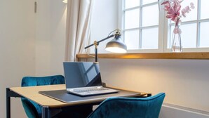 Une pièce moderne avec un ordinateur portable posé sur une table, une lampe de bureau, des chaises de couleur turquoise et une fenêtre avec des rideaux.