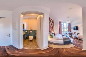Une chambre d’hôtel moderne dotée d’un plancher en bois incurvé, d’un grand lit avec vue, d’un coin salon et d’une salle de bain avec un mur recouvert de carreaux verts.