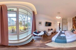 Une chambre d’hôtel moderne dotée d’une fenêtre incurvée, d’un lit, d’un bureau et d’une télévision.