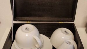 A dark wooden box containing three white cups and saucers. - Homely Stay Studio1 - Your place to relax (München)