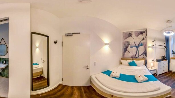 A modern bedroom with a curved bed, a large mirror, and a wall-mounted light fixture. - Homely Stay Studio1 - Your place to relax (München)