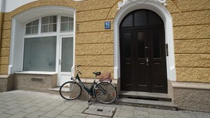 Un edificio con fachada texturizada, un gran ventanal arqueado y una puerta oscura. Una bicicleta está estacionada en la parte delantera.