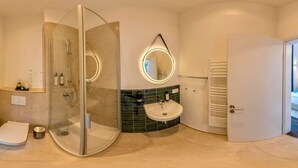 Un baño moderno con ducha de vidrio, espejo redondo, lavamanos y toallero.