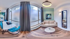 A modern living room with a round window, a sofa, a coffee table, and a dining area with a table and chairs. - Homely Stay Studio6 - Modern with feel-good factor (München)