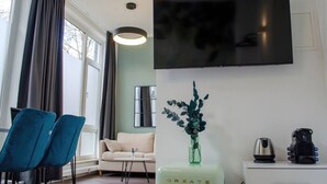A modern living room with a sofa, two blue chairs, a coffee table, a TV mounted on the wall, a decorative vase, and a coffee maker on a cabinet. - Homely Stay Studio6 - Modern with feel-good factor (München)