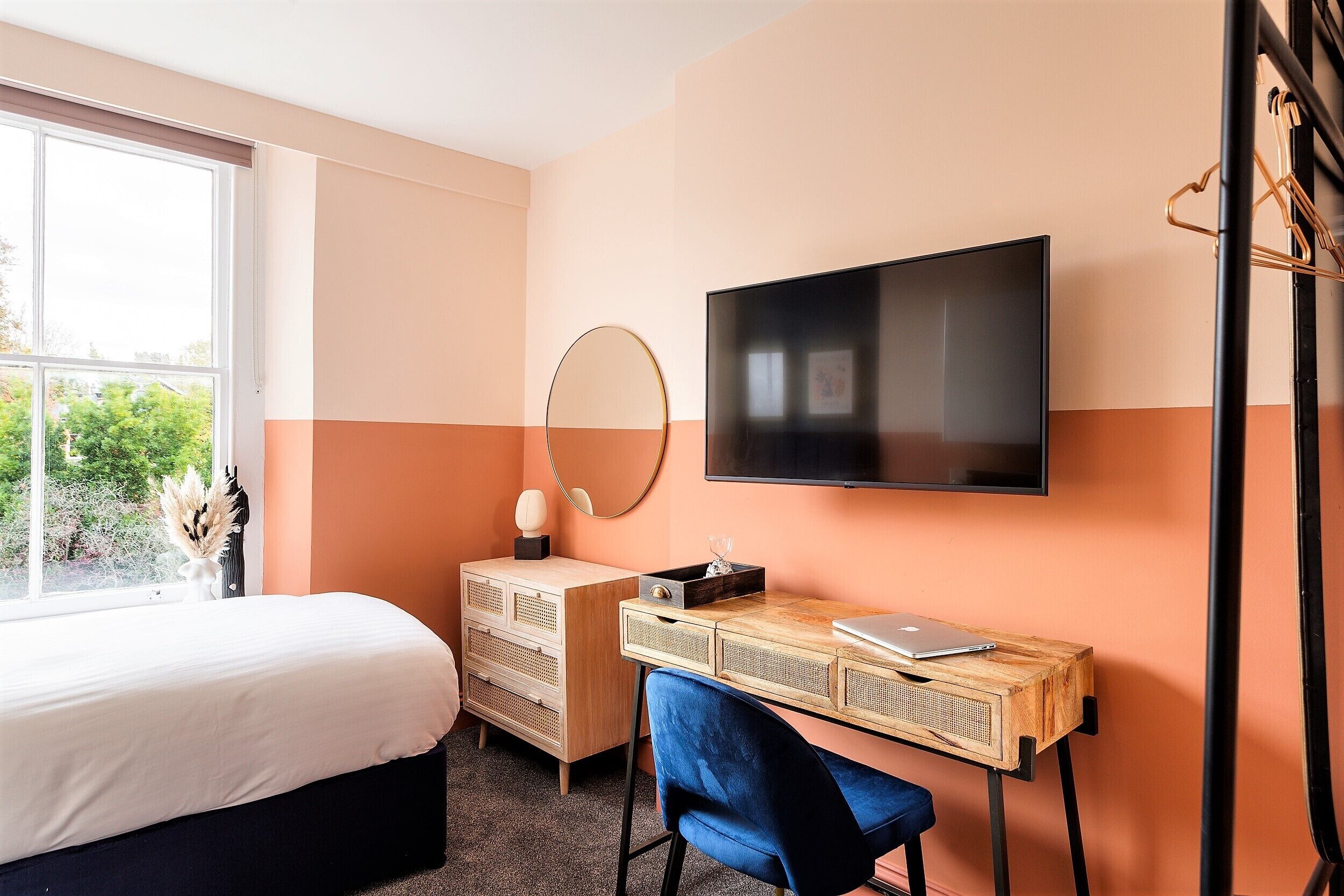 A bedroom with a bed, a desk, a chair, a TV, and a dresser.
