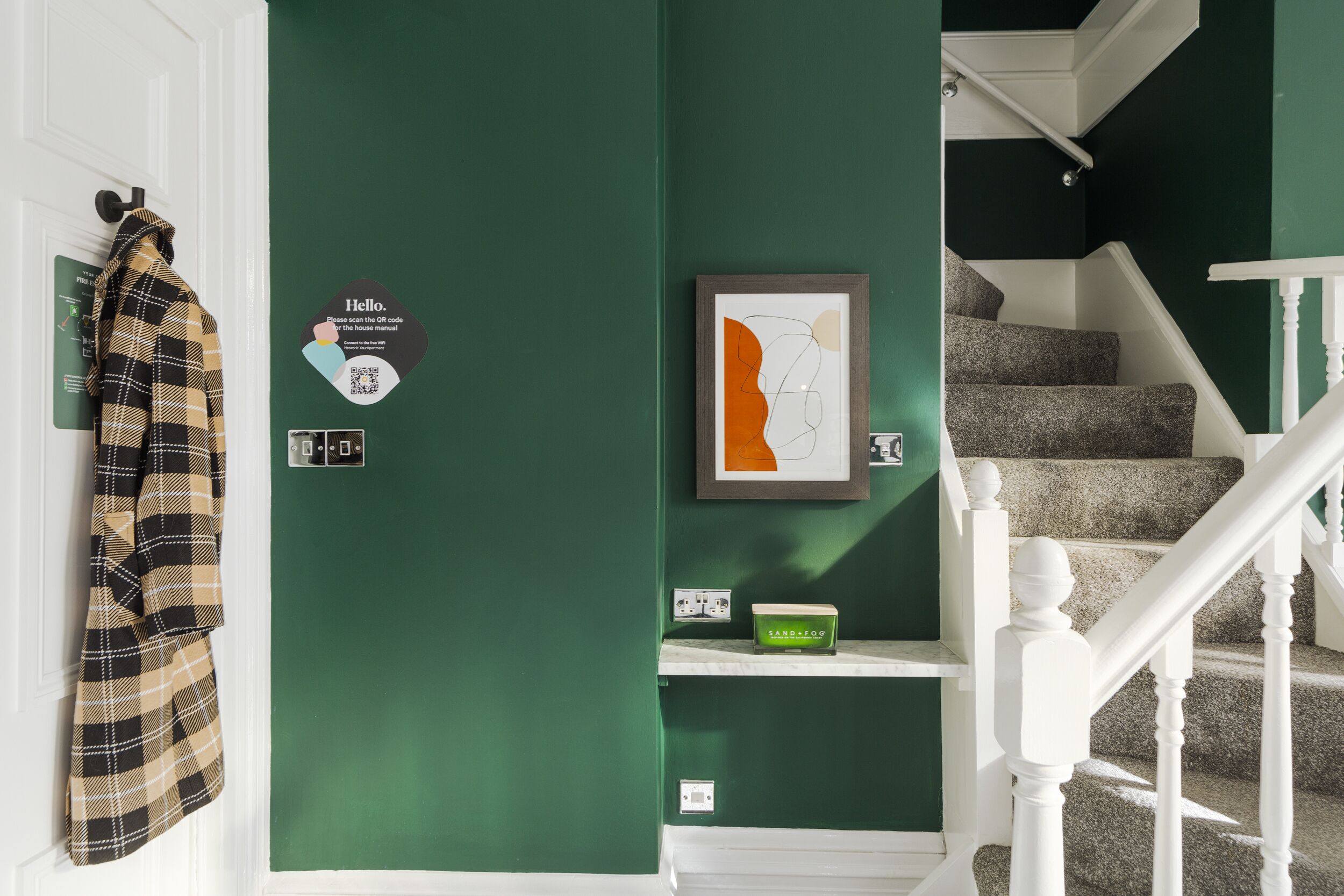 A staircase with white railings and a green wall with a QR code and a framed abstract art piece.