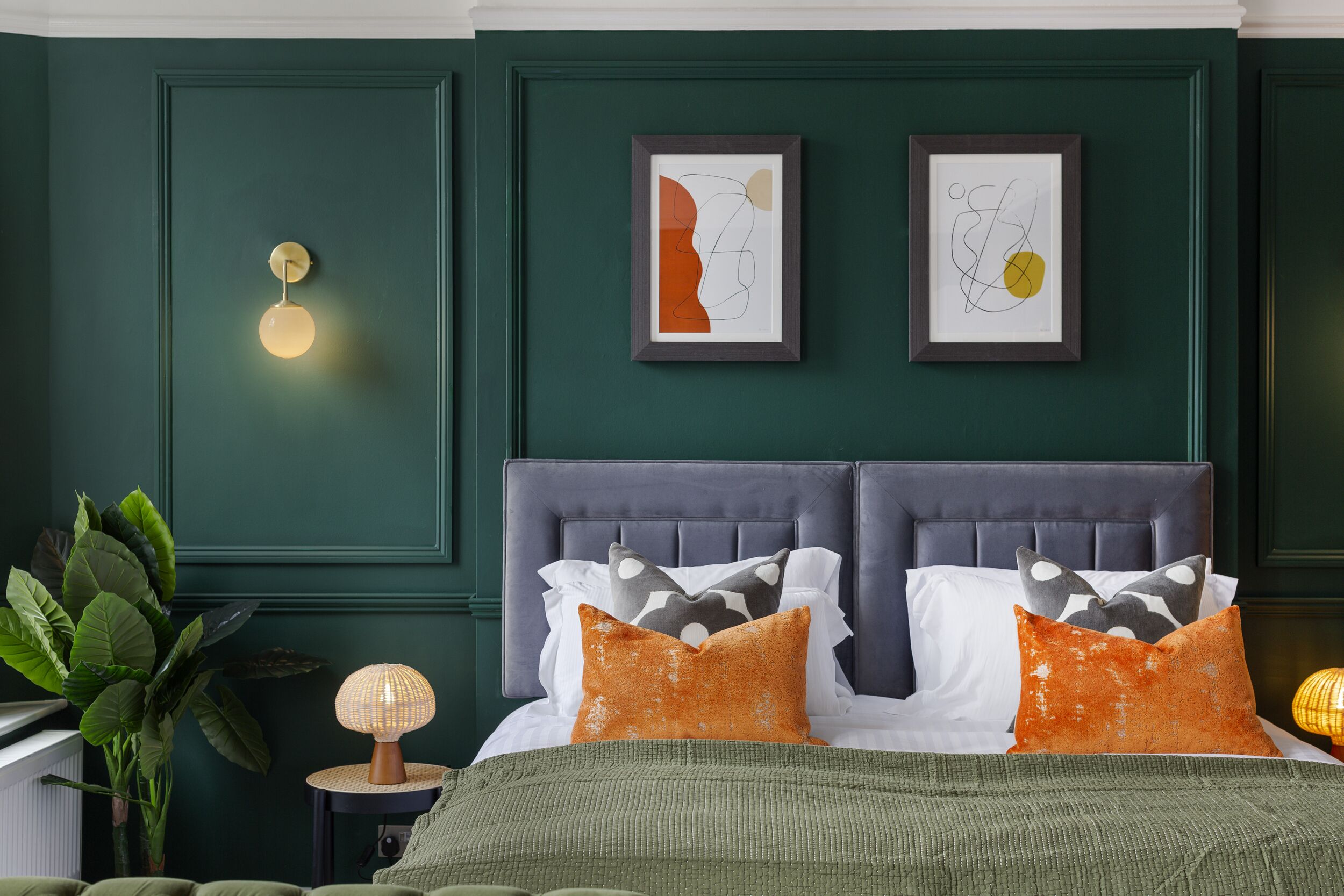 A bedroom with a dark green wall, a tufted headboard, and two framed abstract artworks.