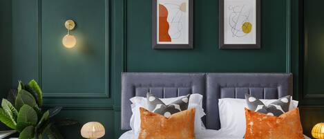 A bedroom with a dark green wall, a tufted headboard, and two framed abstract artworks.