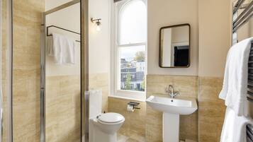 Un baño moderno con cabina de ducha de vidrio, inodoro, lavamanos y ventana con vistas a edificios.