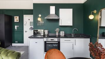 Una cocina compacta con armarios blancos, una campana extractora de acero inoxidable y una encimera negra.