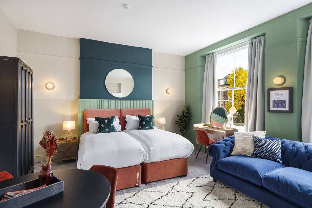 A hotel room with a bed, a blue sofa, a desk, and a window with curtains.