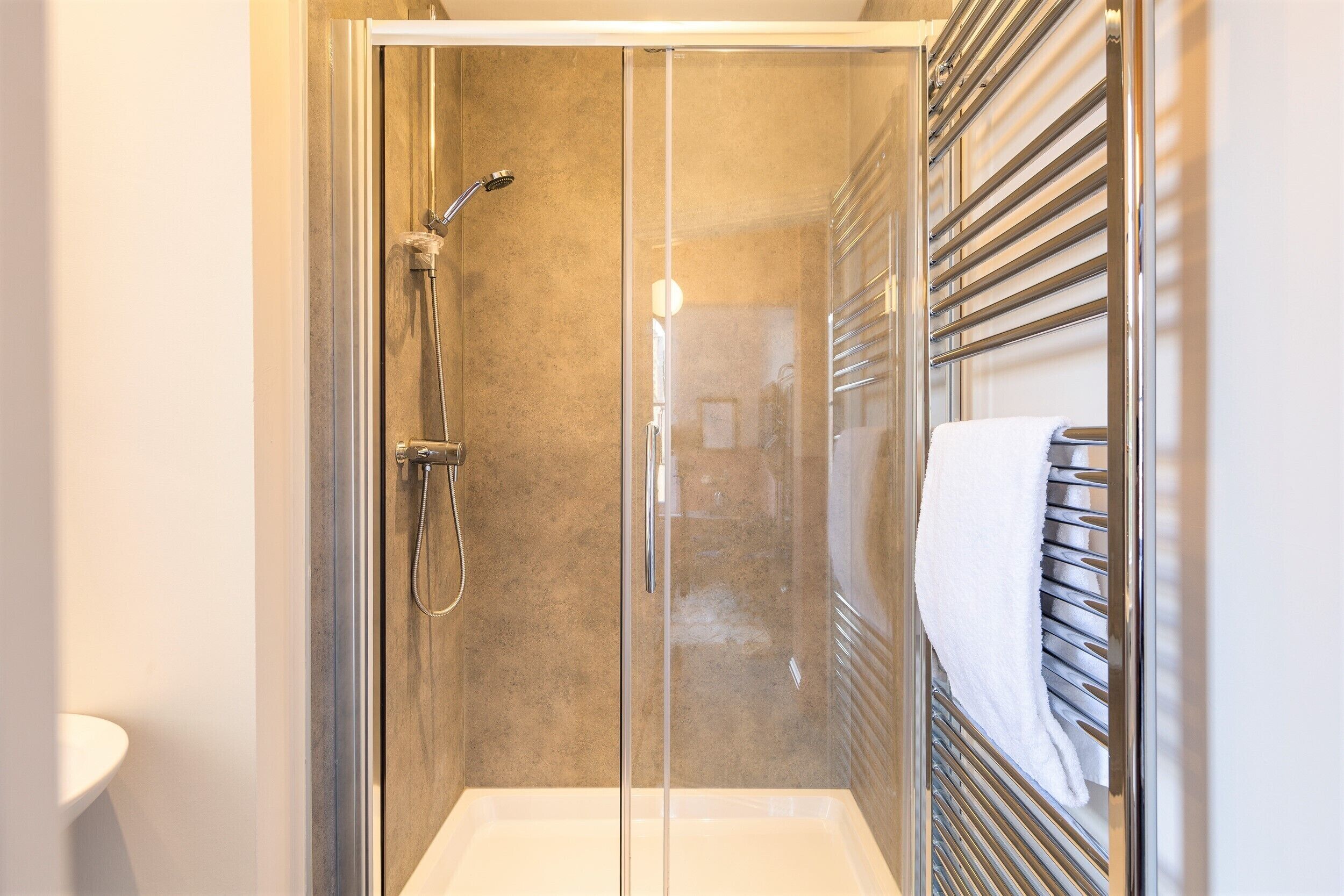 A glass-enclosed shower with a handheld showerhead, a white sink, and a towel rack.