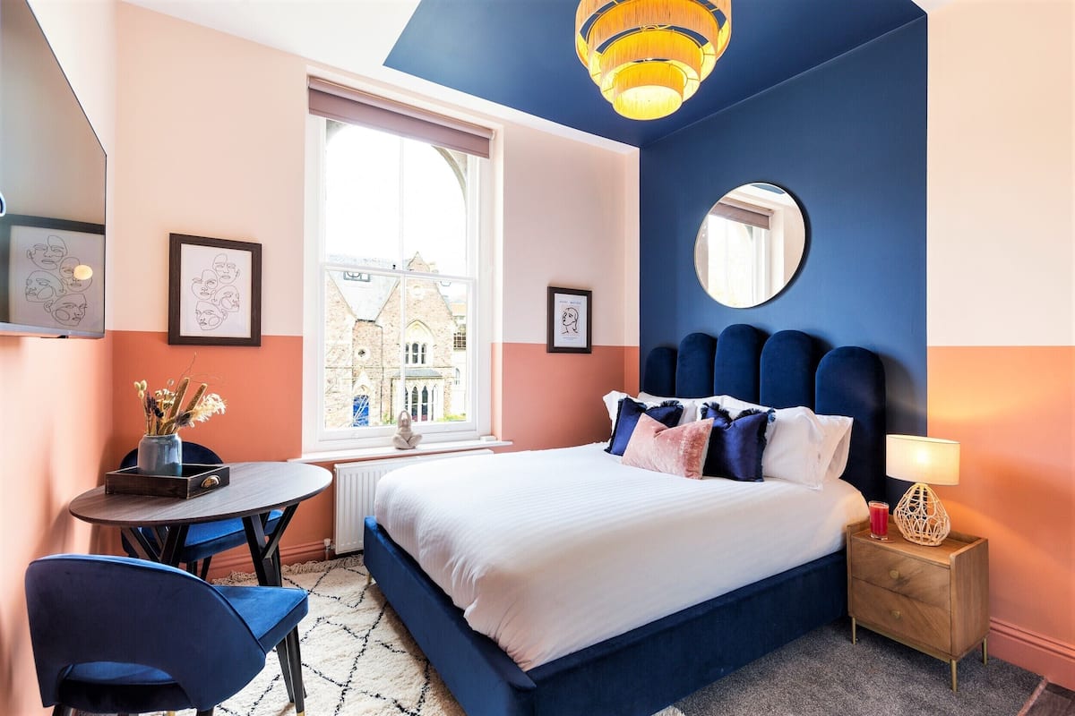 A bedroom with a bed, bedside table, lamp, and a window with a view of a building.